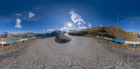 a wide angle 360 - view of a narrow road in the mountains with a mountain behind it