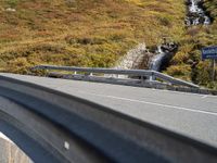 a highway in the middle of the mountains with a waterfall coming down it, beside a winding road