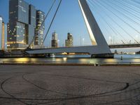 a large bridge that spans across the water and to the surrounding buildings and a park bench at the end