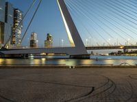 a large bridge that spans across the water and to the surrounding buildings and a park bench at the end