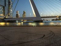 a large bridge that spans across the water and to the surrounding buildings and a park bench at the end