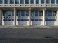 a large building that is sitting outside in the sun, all cement and glass, with rows of windows and concrete pillars