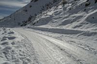 a snowy slope and a road with many snow covered tracks on it and one person on skis is snowboarding on the slope, with skis