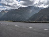 a motorcycle is on the empty road during the day next to some mountains, some trees and water