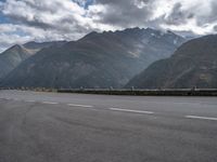 a motorcycle is on the empty road during the day next to some mountains, some trees and water