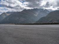 a motorcycle is on the empty road during the day next to some mountains, some trees and water