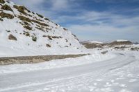 a large snowy area next to a road with tracks in it and mountains in the distance