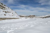 a large snowy area next to a road with tracks in it and mountains in the distance