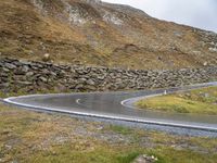 there is a curved, curving road with rocks on the hill side and grassy grass in the middle