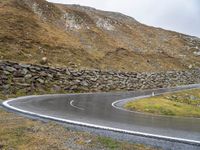 there is a curved, curving road with rocks on the hill side and grassy grass in the middle