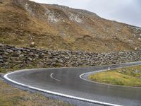 there is a curved, curving road with rocks on the hill side and grassy grass in the middle