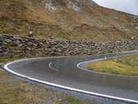 there is a curved, curving road with rocks on the hill side and grassy grass in the middle