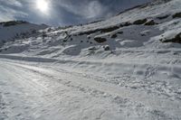 a man riding down a snow covered mountain next to rocks and a dirt road with skis on it