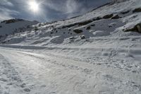 a man riding down a snow covered mountain next to rocks and a dirt road with skis on it