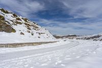 snow covered trail that runs through the road and a mountain behind it with footprints in the white snow