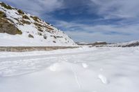 snow covered trail that runs through the road and a mountain behind it with footprints in the white snow