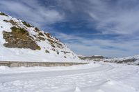 snow covered trail that runs through the road and a mountain behind it with footprints in the white snow