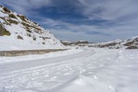 snow covered trail that runs through the road and a mountain behind it with footprints in the white snow