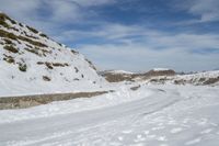 snow covered trail that runs through the road and a mountain behind it with footprints in the white snow