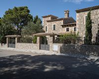 a large house with stone and stucco walls and a fence that extends the front yard