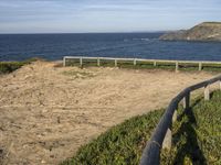 wooden fence and dirt path leading to beach by sea with blue sky above with mountains in background