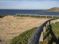 wooden fence and dirt path leading to beach by sea with blue sky above with mountains in background