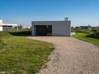 the empty building sits on a grassy area beside a road with gravel in front of it