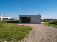 the empty building sits on a grassy area beside a road with gravel in front of it