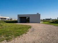 the empty building sits on a grassy area beside a road with gravel in front of it