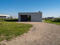 the empty building sits on a grassy area beside a road with gravel in front of it