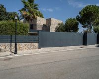 a black metal fence that separates the street with a brick building in the background and palm trees behind it