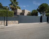 a black metal fence that separates the street with a brick building in the background and palm trees behind it