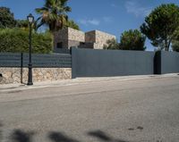 a black metal fence that separates the street with a brick building in the background and palm trees behind it