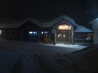 the entrance to a small building at night with snow covering the ground around it and a snow drifting onto the ground underneath