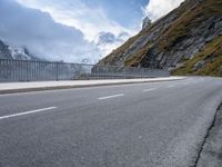 a road with an empty and steep mountain in the background on a cloudy day with blue sky