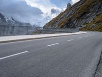 a road with an empty and steep mountain in the background on a cloudy day with blue sky