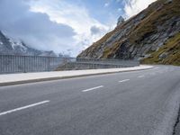 a road with an empty and steep mountain in the background on a cloudy day with blue sky