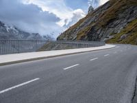 a road with an empty and steep mountain in the background on a cloudy day with blue sky