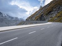 a road with an empty and steep mountain in the background on a cloudy day with blue sky