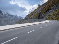 a road with an empty and steep mountain in the background on a cloudy day with blue sky