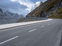 a road with an empty and steep mountain in the background on a cloudy day with blue sky