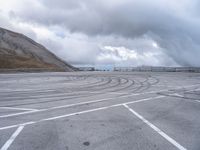 a car driving around a curve in an empty lot on a cloudy day with large mountains in the background