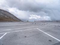 a car driving around a curve in an empty lot on a cloudy day with large mountains in the background