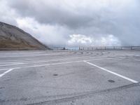 a car driving around a curve in an empty lot on a cloudy day with large mountains in the background