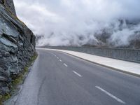 a paved road that has fog rising from it with clouds above the mountains in the background