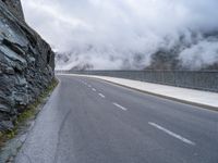 a paved road that has fog rising from it with clouds above the mountains in the background