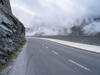 a paved road that has fog rising from it with clouds above the mountains in the background