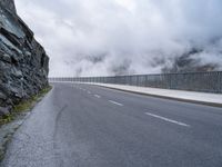 a paved road that has fog rising from it with clouds above the mountains in the background