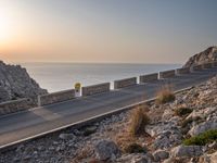 the empty highway on the side of a cliff in the sunset overlooking a body of water