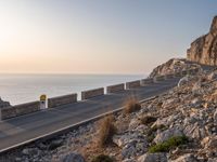 the empty highway on the side of a cliff in the sunset overlooking a body of water